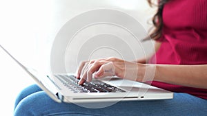 Close up of a young woman s hands typing on a keyboard of a computer that is on her lap