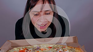 Close up of young woman sniffing appetizing large pizza in box. Happy female in anticipation after diet enjoying