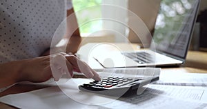 Close up young woman summarizing payments with calculator.