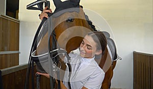 CLOSE UP: Young woman tacking up and putting a bridle on her beautiful horse.