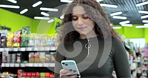 Close up young woman use smartphone in supermarket. Woman buyer using mobile phone application standing with shopping
