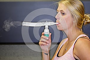 A close up of a young woman using a nebulizer kit.
