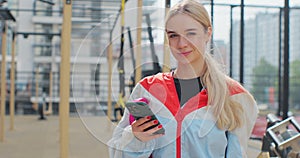 Close up of young woman using smartphone checking fitness applications standing at sport ground. Healthy lifestyle