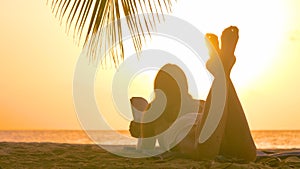 CLOSE UP: Young woman on vacation in Barbados reads on a sandy beach at sunset.