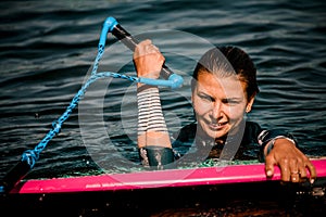 Close-up of young woman in wetsuit in water with surf style wakeboard and holding rope