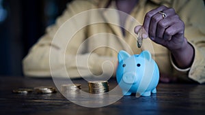 Close up young women put coins into a blue piggy bank sitting at a desk finance health insurance health money saving