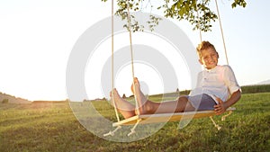 CLOSE UP Youngster relaxing on a wooden swing at sunset,posing for the camera. photo