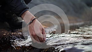 Close-up on your hands. A hiker puts his hand down into a cold river. Close-up.