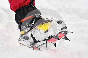 Close up of â€Žmountaineering crampons with visible sharp teeth on a foot with gaiters, on snow. Winter hiking, equipment, gear