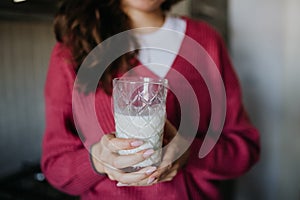 Close upf of woman holding glass with plant-based milk in the kitchen.