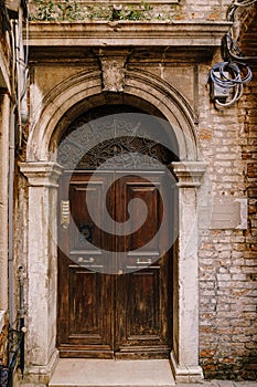 Close-ups of building facades in Venice, Italy. An old, gloomy wooden door, brown. Stone arched doorway. The facade of a