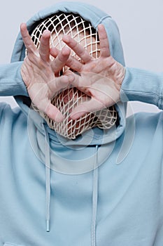 a close vertical, conceptual studio photograph of a strange, tortured man in a light blue hoodie covering his face with