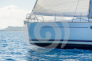 Close view against the sun at sailboat bow with hoisted headsail.