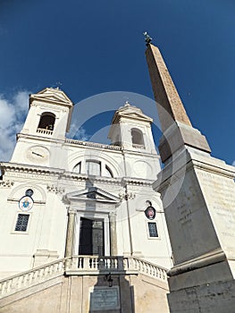 A close view of the bright white church Trinita dei Monti with the obelisk in front of it