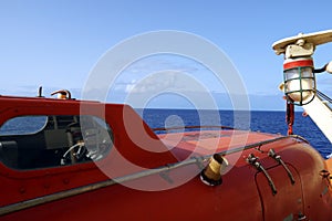 Close view on cabin of the orange colour life boat with reflective tape stickers secured with davits and safety hooks.