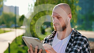 Close view of the caucasian male student using digital tablet, texting, scrolling apps using earphones sitting on a