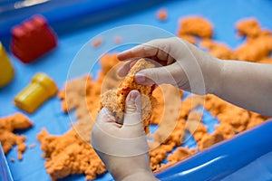 Close view of child`s hands playing with kinetic sand.