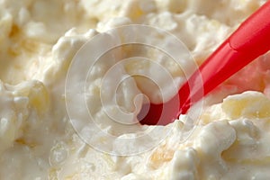 Close view cottage cheese and pineapple chunks with a red plastic spoon in the food