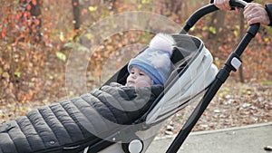 Close view of a cute baby in a stroller who is on a walk with his parents in a cozy city park. Dad and mom ride on