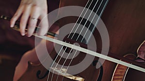 Close view of female violoncellist playing on the strings with fiddlestick