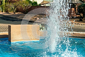 Close view of foutain with small beige exterior retaining wall and spraying water spout or hose in water in sunlight