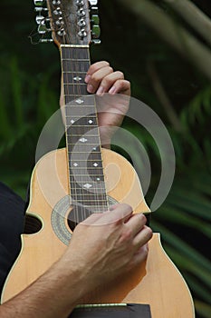 Close view of hands playing a Cuatro guitar.