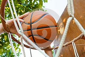 Close view of hands throwing a ball into a basketball basket, teenage boy playing at home in the backyard, outdoor activities on