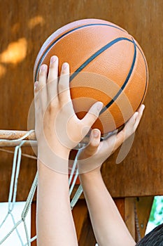 Close view of hands throwing a ball into a basketball basket, teenage boy playing at home in the backyard, outdoor activities on