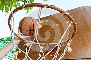 Close view of hands throwing a ball into a basketball basket, teenage boy playing at home in the backyard, outdoor activities on