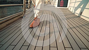 Close view of a man's legs in orange boots walking on a wooden deck boat