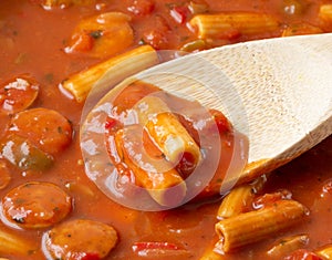 Close view of rigatoni pasta and sausage with a wood spoon