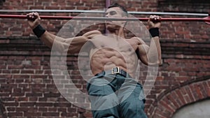 Close view of strong sportsman doing pull ups on horizontal bar outdoors