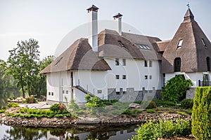 A close view of a structure with an authentic roof with white walls, smokers and a spire at the top. House by the river