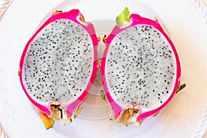 Close view of two cut white dragon fruit showing pink rind and black seeds, centered on plate