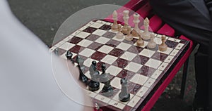 Close view of two seniors friends playing the chess on street bench on leisure