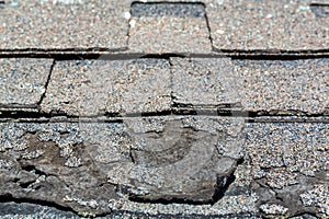 Close view of weathered shingles with a layer curled and damaged from the sun