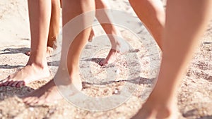 Close view of women tanned legs and feet walking on sandy beach to the ocean on sunny day. Slim pretty girls go by the