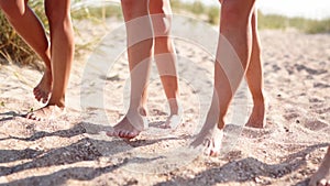 Close view of women tanned legs and feet walking on sandy beach to the ocean on sunny day. Slim pretty girls go by the
