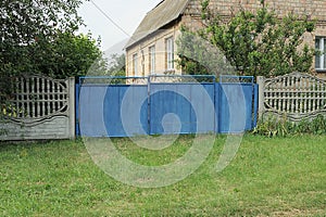 Closed blue metal gate and door near the gray concrete wall