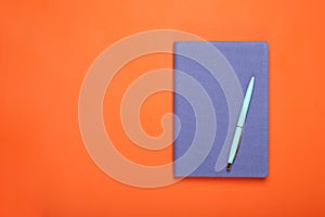 Closed blue notebook and pen on orange background, top view. Space for text