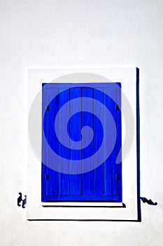 Closed blue window on a white wall in cycladic style