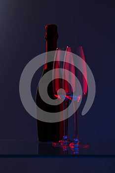 Closed bottle of champagne with two empty glasses. Blue-red color.