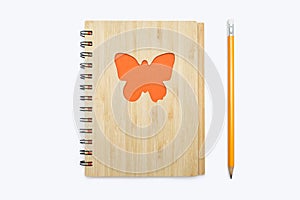 Closed bound notebook with a babmouk cover with an orange butterfly ornament on a white background and a yellow pencil