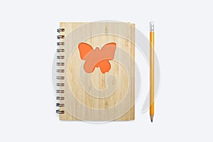 Closed bound notebook with a babmouk cover with an orange butterfly ornament on a white background and a yellow pencil