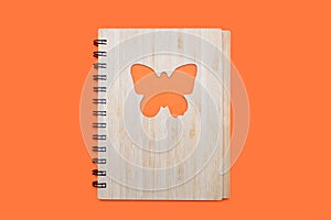 Closed bound notebook with a bamboo cover with a butterfly ornament on an orange background