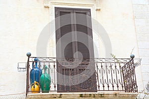 Closed brown door with green, blue and yellow vases on a balcony in south Italy