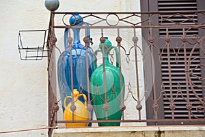 Closed brown door with green, blue and yellow vases on a balcony in south Italy