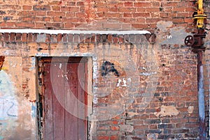 Closed brown painted door, red brick wall with yellow rusty gas pipe with spigot