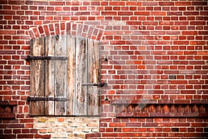 Closed brown red wooden window with rusted metal hinges on a grungy red brick wall