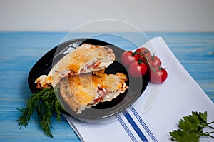 Closed calzone pizza on a wooden table with fresh tomatoes and d